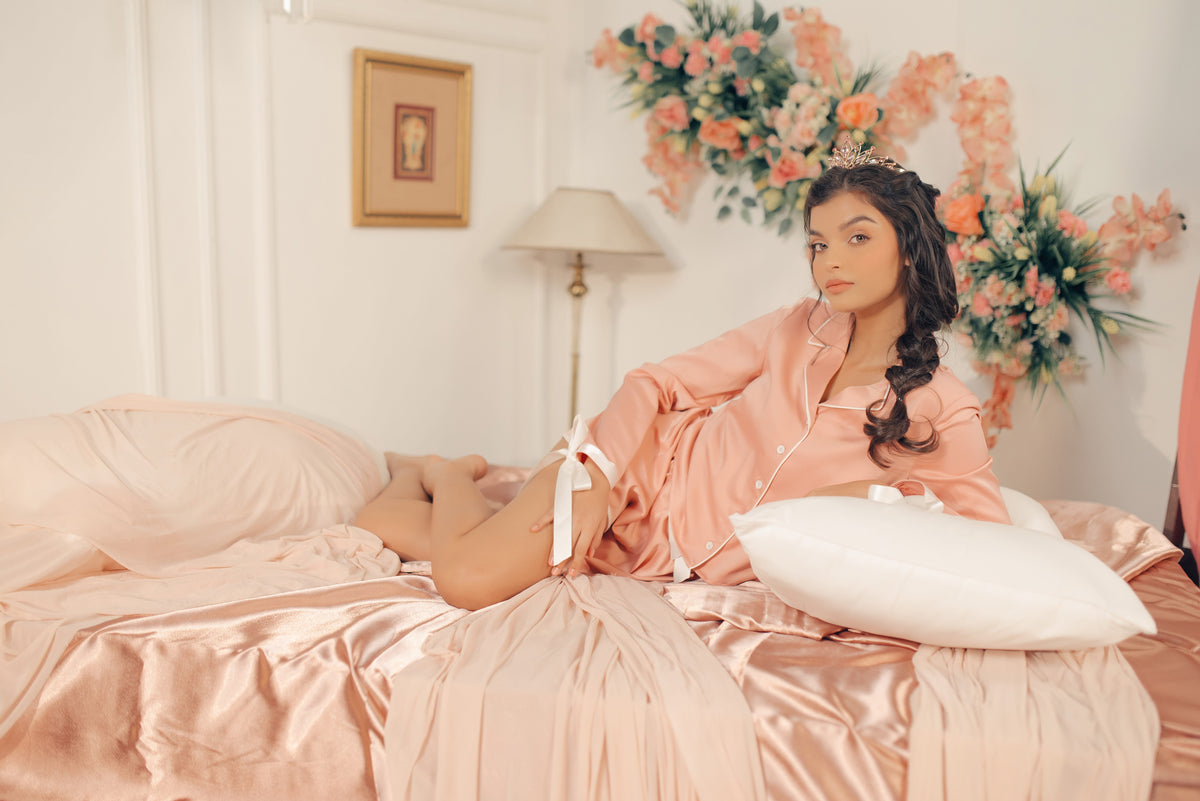 Woman in pink pajamas sitting on a bed with floral decorations in the background